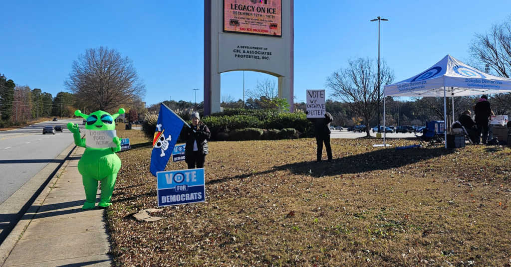 Douglas County Democrats waving signs for donations in front of Arbor Place Mall on Black Friday 2025