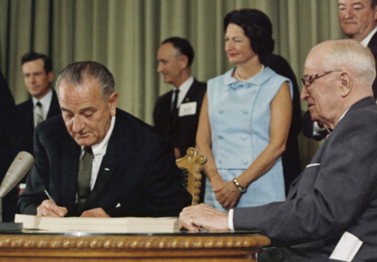 President Johnson signs the Medicare bill in the presence of Harry Truman, who had tried to get medical insurance for the elderly when he was President.